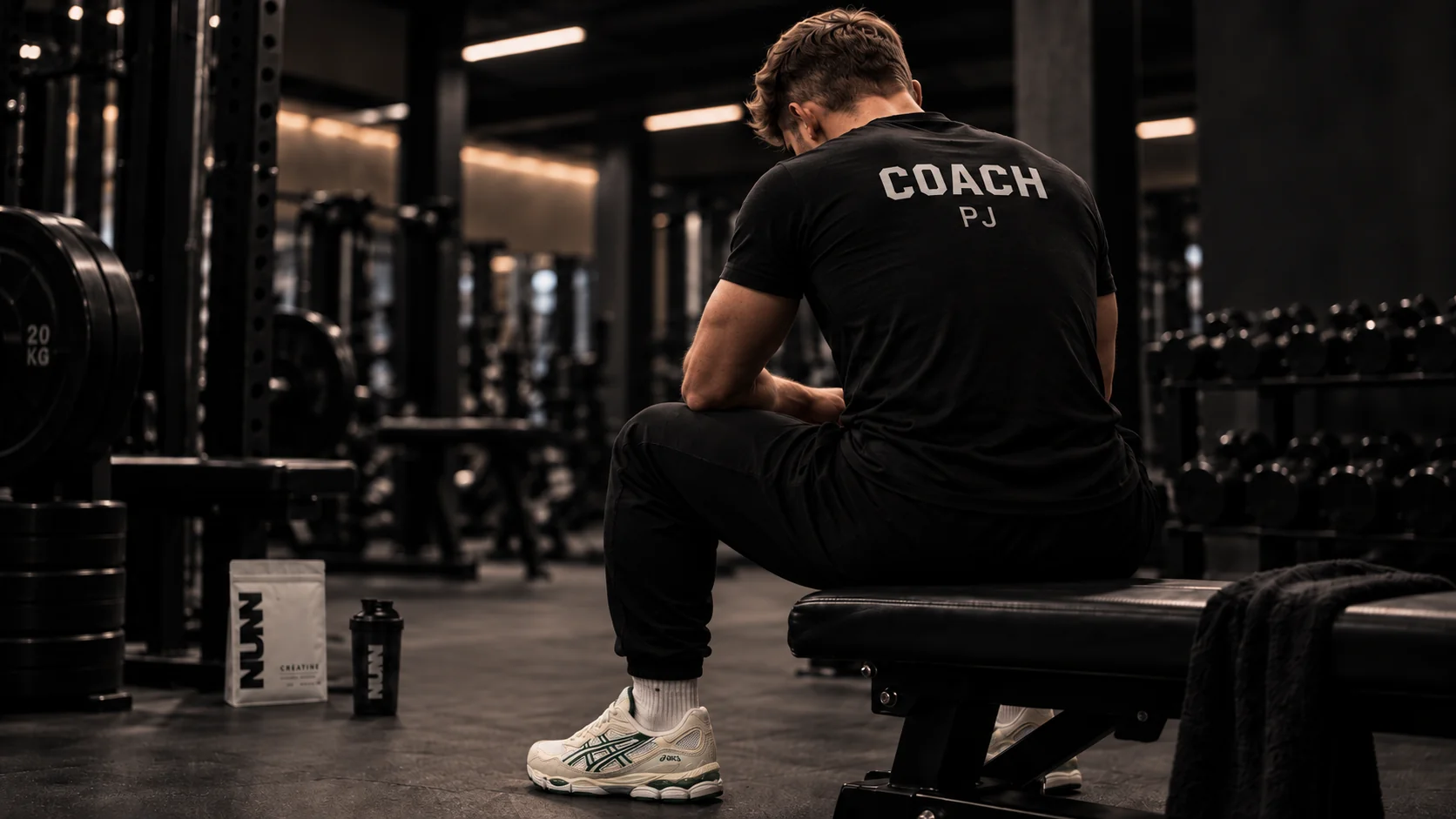 Pierre-Jules, de dos, assis sur un banc dans la salle de sport, avec COACH PJ inscrit sur son t-shirt